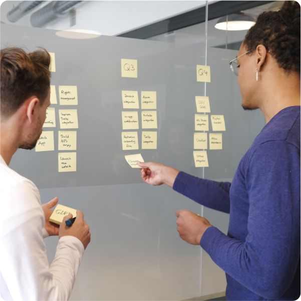 Team members adding sticky notes to a board planning quarterly goals for software development Team members adding sticky notes to a board planning quarterly goals for software development